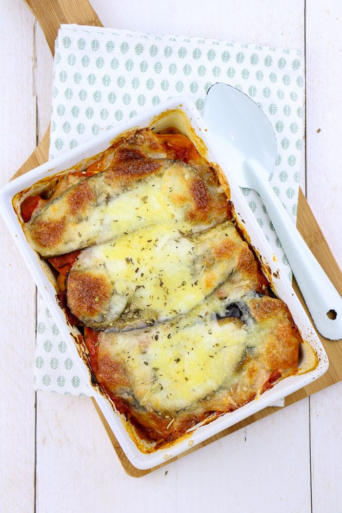 Zoete aardappel lasagne met spinazie, aubergine, en paprika, vers uit de oven, geserveerd in een ovenschaal met een knapperige korstje van mozzarella en kleurrijke lagen van verse groenten.