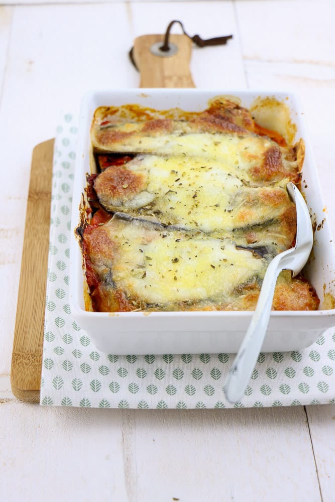 Zoete aardappel lasagne met spinazie, aubergine, en paprika, vers uit de oven, geserveerd in een ovenschaal met een knapperige korstje van mozzarella en kleurrijke lagen van verse groenten.