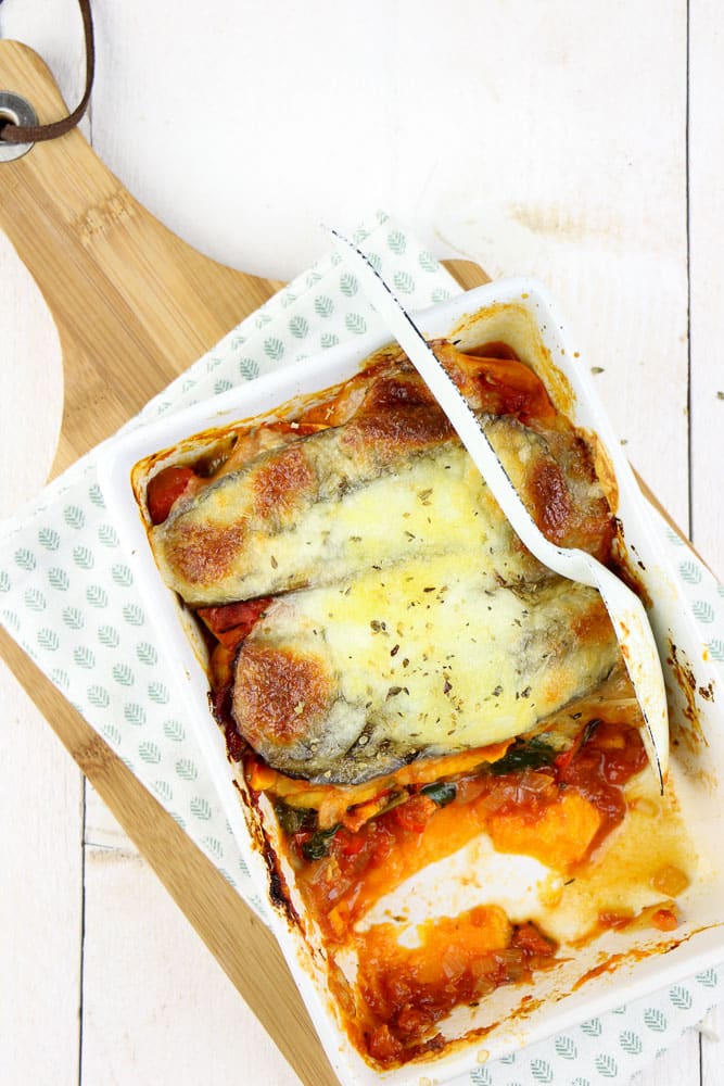 Zoete aardappel lasagne met spinazie, aubergine, en paprika, vers uit de oven, geserveerd in een ovenschaal met een knapperige korstje van mozzarella en kleurrijke lagen van verse groenten.