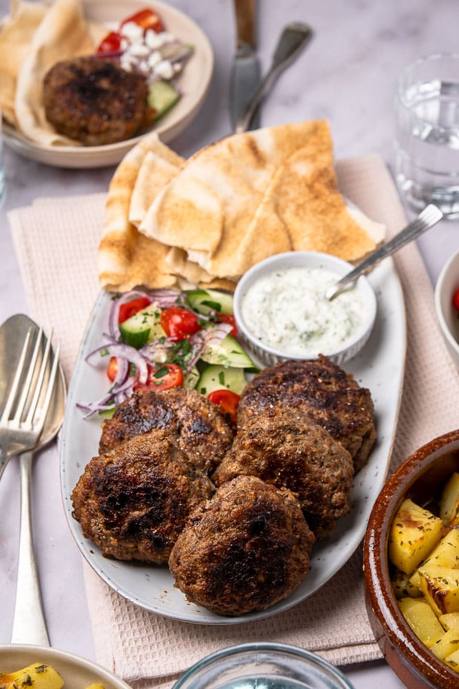 Traditionele Griekse bifteki gehaktballen recept, gerecht met gehakt, tomaat, ui en verse kruiden en geserveerd met tzatziki saus en een frisse Griekse salade.