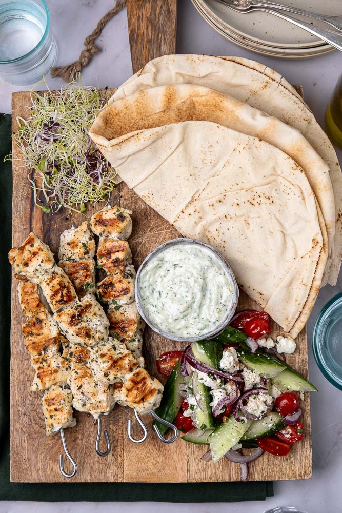 Een heerlijk recept voor gegrilde souvlaki spiesen van kip, geserveerd met pita, frisse Griekse salade, en een schaaltje zelfgemaakte tzatziki, perfect voor een zomerse maaltijd in de Mediterrane stijl.