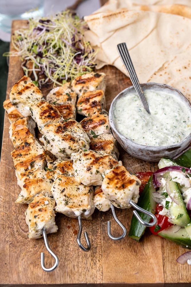 Een heerlijk recept voor gegrilde souvlaki spiesen van kip, geserveerd met pita, frisse Griekse salade, en een schaaltje zelfgemaakte tzatziki, perfect voor een zomerse maaltijd in de Mediterrane stijl.