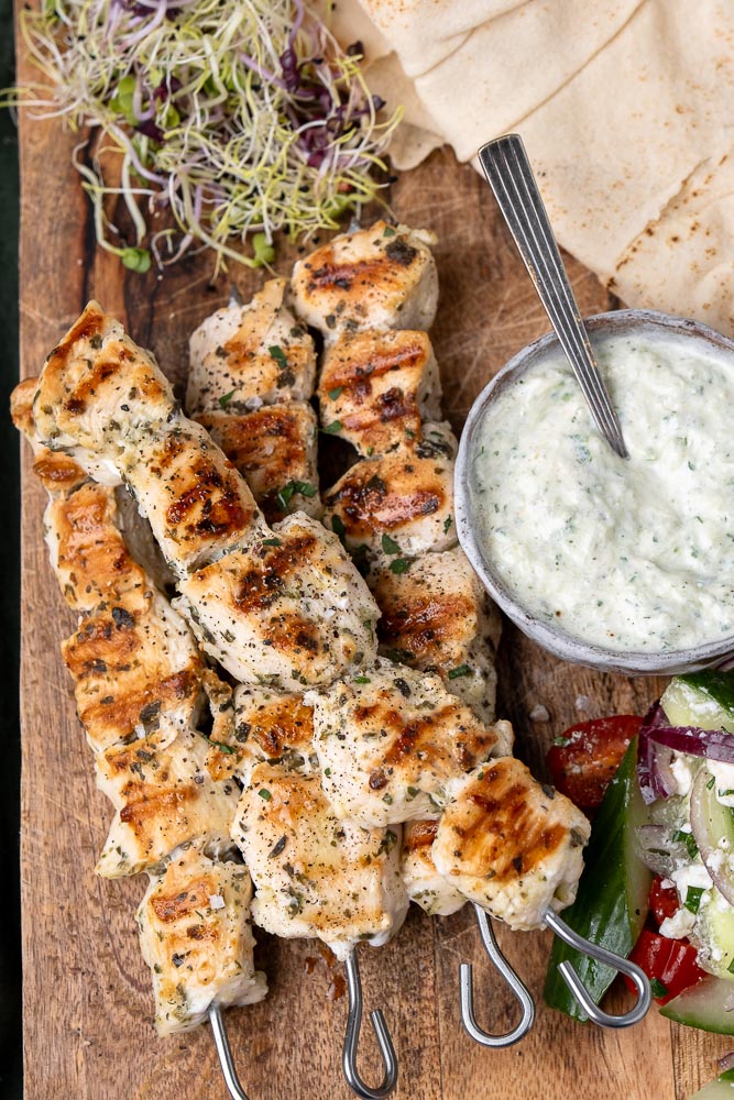 Een heerlijk recept voor gegrilde souvlaki spiesen van kip, geserveerd met pita, frisse Griekse salade, en een schaaltje zelfgemaakte tzatziki, perfect voor een zomerse maaltijd in de Mediterrane stijl.