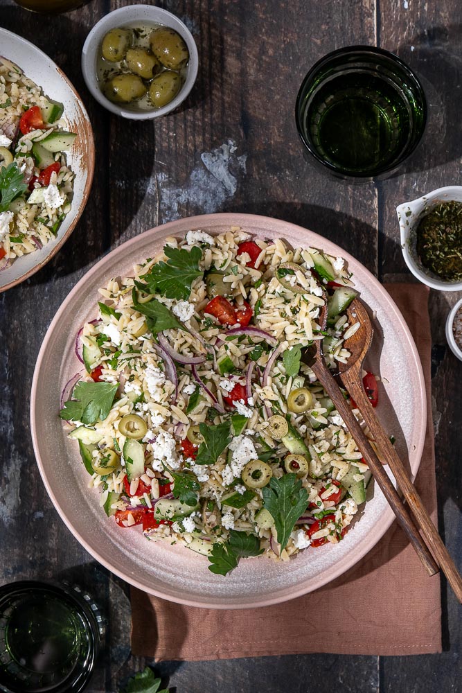 Kleurrijke Griekse pasta salade in een kom. Ontdek de heerlijke smaken van een Griekse orzo salade, een frisse en gezonde keuze voor elke maaltijd. Perfect als bijgerecht of hoofdgerecht met ingrediënten zoals feta, olijven, tomaat en komkommer. Ideaal voor zomerse dagen!