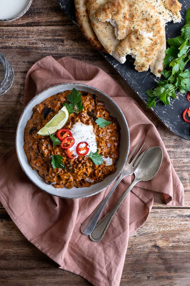 Vegetarische aubergine curry met linzen, geserveerd met verse koriander en naanbrood, romige Indiase curry met kokosmelk en groenten.