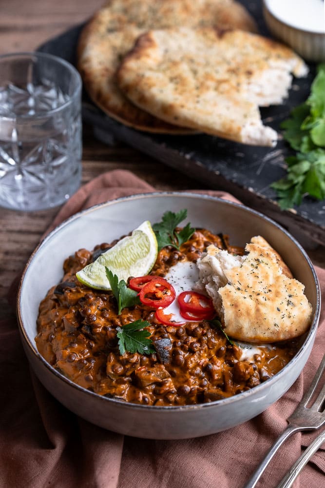 Vegetarische aubergine curry met linzen, geserveerd met verse koriander en naanbrood, romige Indiase curry met kokosmelk en groenten.