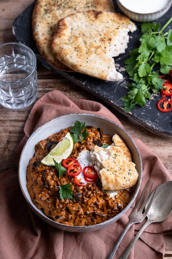 Vegetarische aubergine curry met linzen, geserveerd met verse koriander en naanbrood, romige Indiase curry met kokosmelk en groenten.