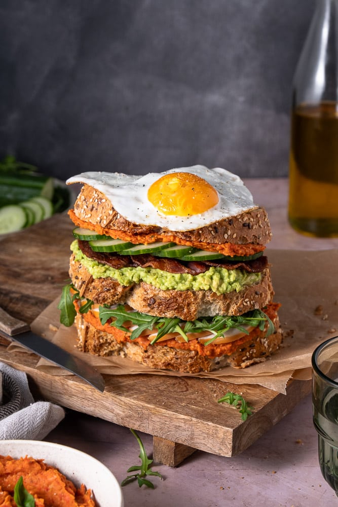 Rijkelijk belegde club sandwich met kip, bacon, avocado en een gebakken eitje, geserveerd op geroosterd volkoren brood voor een luxe lunch.