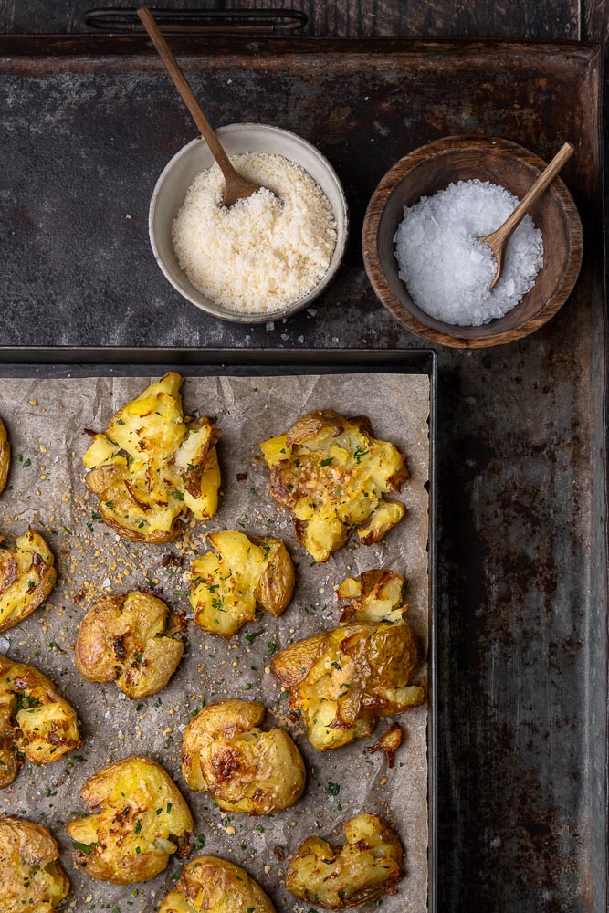 Krokante smashed potatoes uit de oven met een topping van knoflookboter en Parmezaanse kaas, bijgerecht van krokante aardappels uit de oven, feestelijk bijgerecht, Kerst, Pasen, knapperige aardappel uit de oven. 