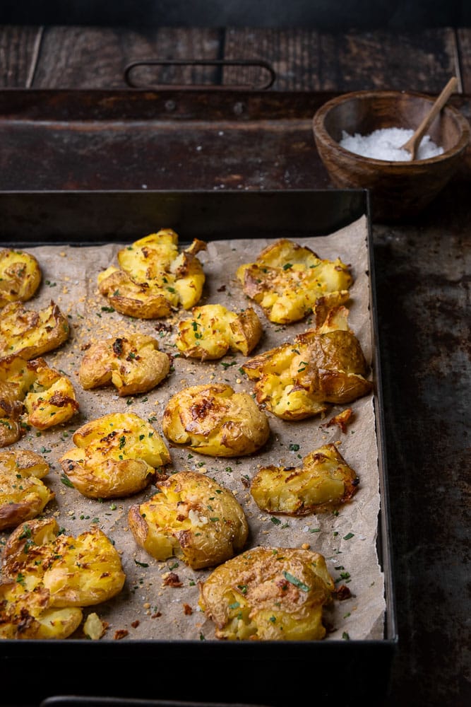 Krokante smashed potatoes uit de oven met een topping van knoflookboter en Parmezaanse kaas, bijgerecht van krokante aardappels uit de oven, feestelijk bijgerecht, Kerst, Pasen, knapperige aardappel uit de oven. 