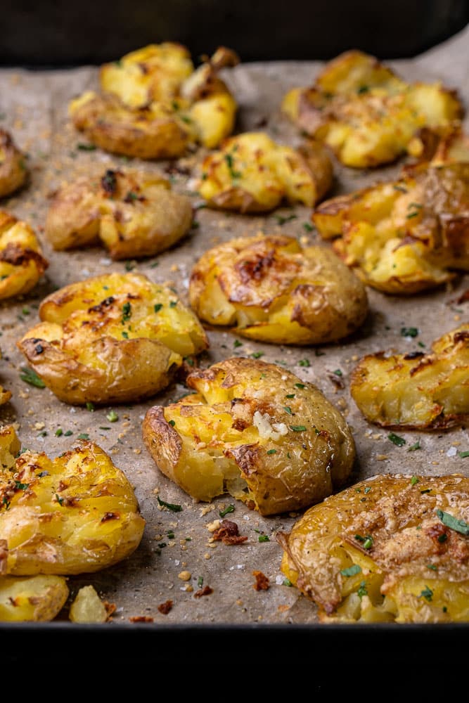 Krokante smashed potatoes uit de oven met een topping van knoflookboter en Parmezaanse kaas, bijgerecht van krokante aardappels uit de oven, feestelijk bijgerecht, Kerst, Pasen, knapperige aardappel uit de oven. 