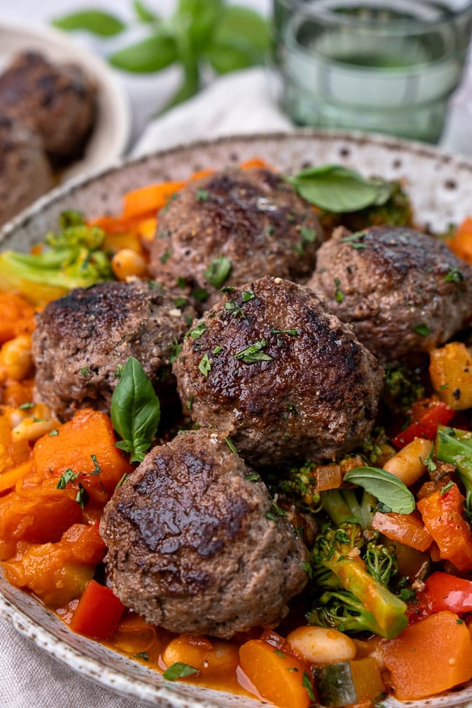 Makkelijk recept voor gezonde groenteschotel met paprika, courgette, pompoen, broccoli en bospeen, geserveerd met kruidige gehaktballen en witte bonen als complete en gezonde maaltijd.