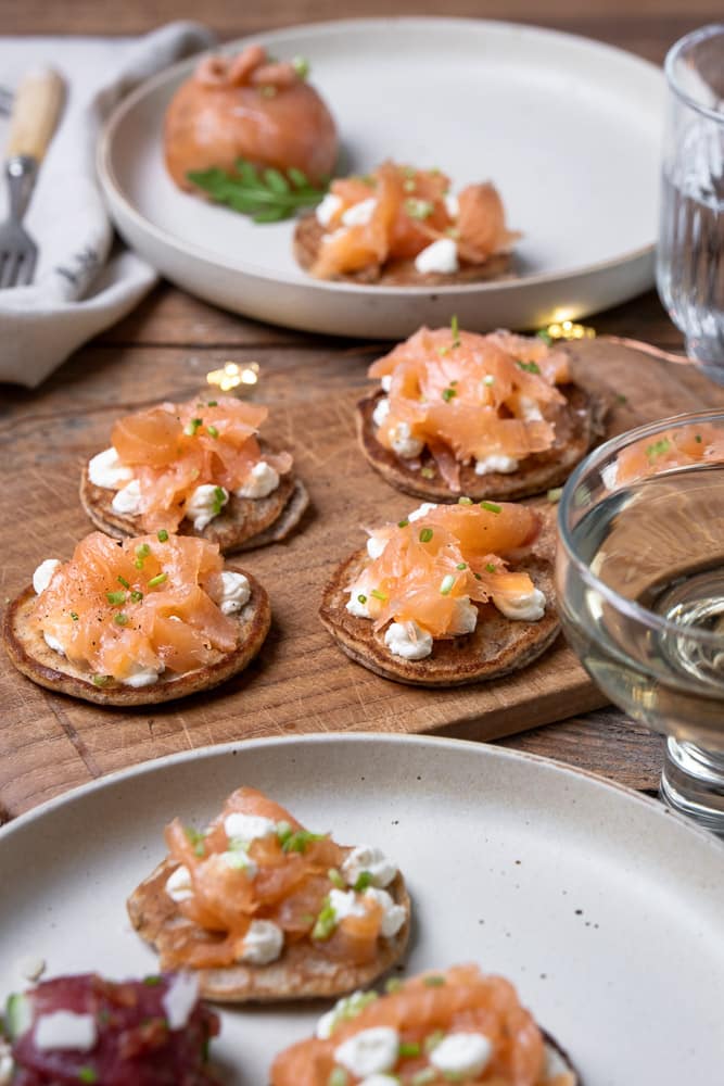 Blini’s met gerookte zalm, crème fraîche, bieslook en amandelmeel als basis, geserveerd als feestelijk koolhydraatarm hapje of voorgerecht. Glutenvrij blini recept, koolhydraatarme blini, blini met zalm recept.