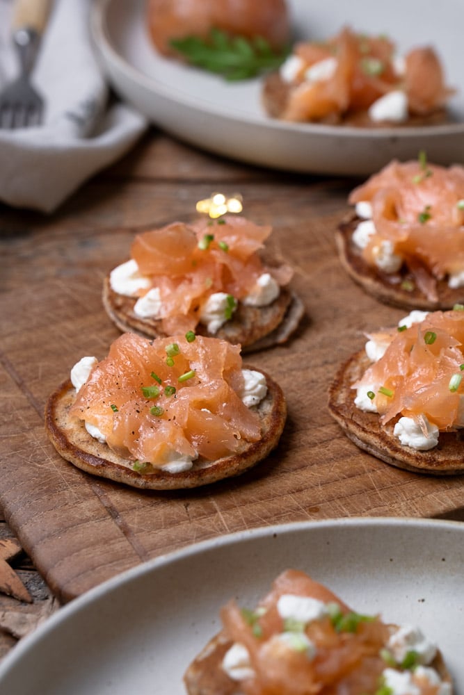 Blini’s met gerookte zalm, crème fraîche, bieslook en amandelmeel als basis, geserveerd als feestelijk koolhydraatarm hapje of voorgerecht. Glutenvrij blini recept, koolhydraatarme blini, blini met zalm recept.