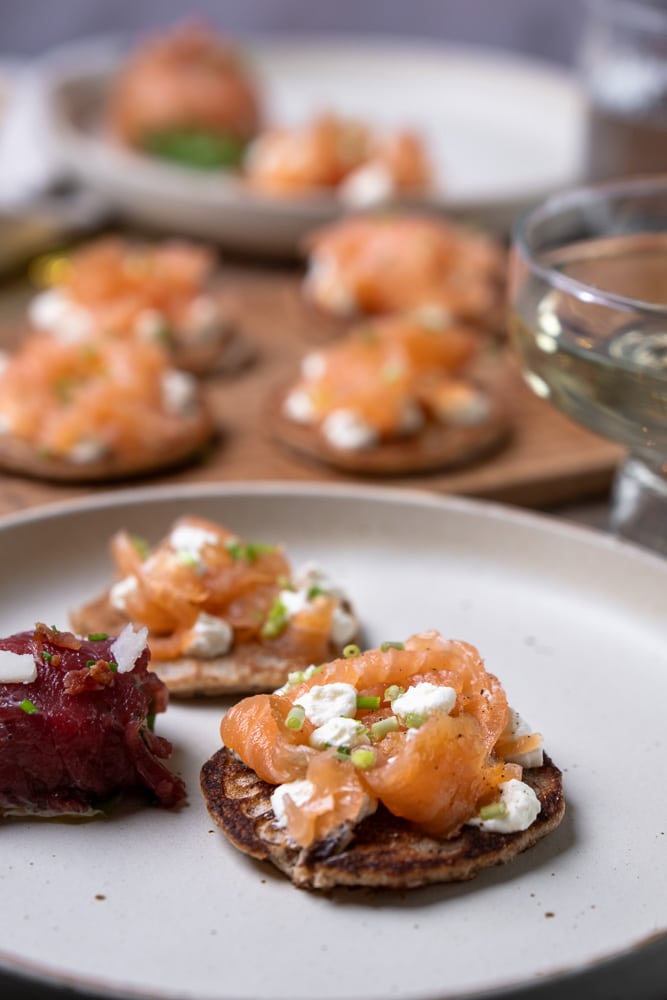 Blini’s met gerookte zalm, crème fraîche, bieslook en amandelmeel als basis, geserveerd als feestelijk koolhydraatarm hapje of voorgerecht. Glutenvrij blini recept, koolhydraatarme blini, blini met zalm recept.